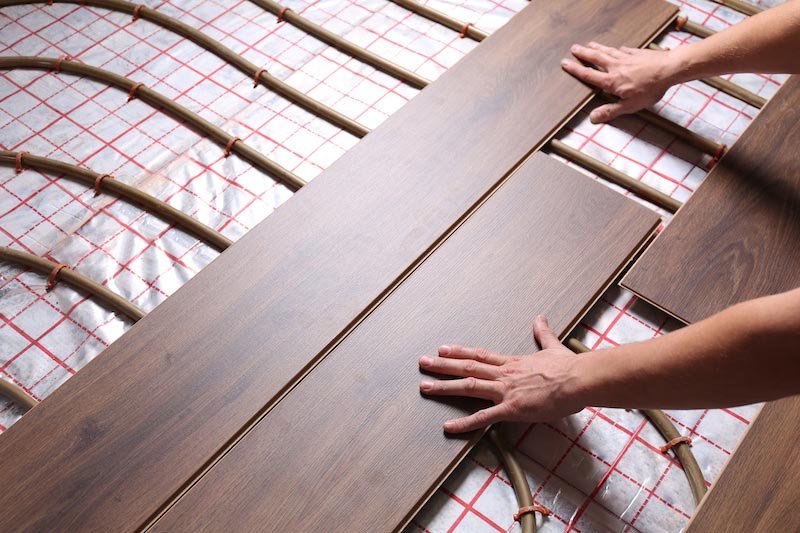 Worker installing new wooden laminate over underfloor heating sy Worker installing new wooden laminate over underfloor heating system, closeup